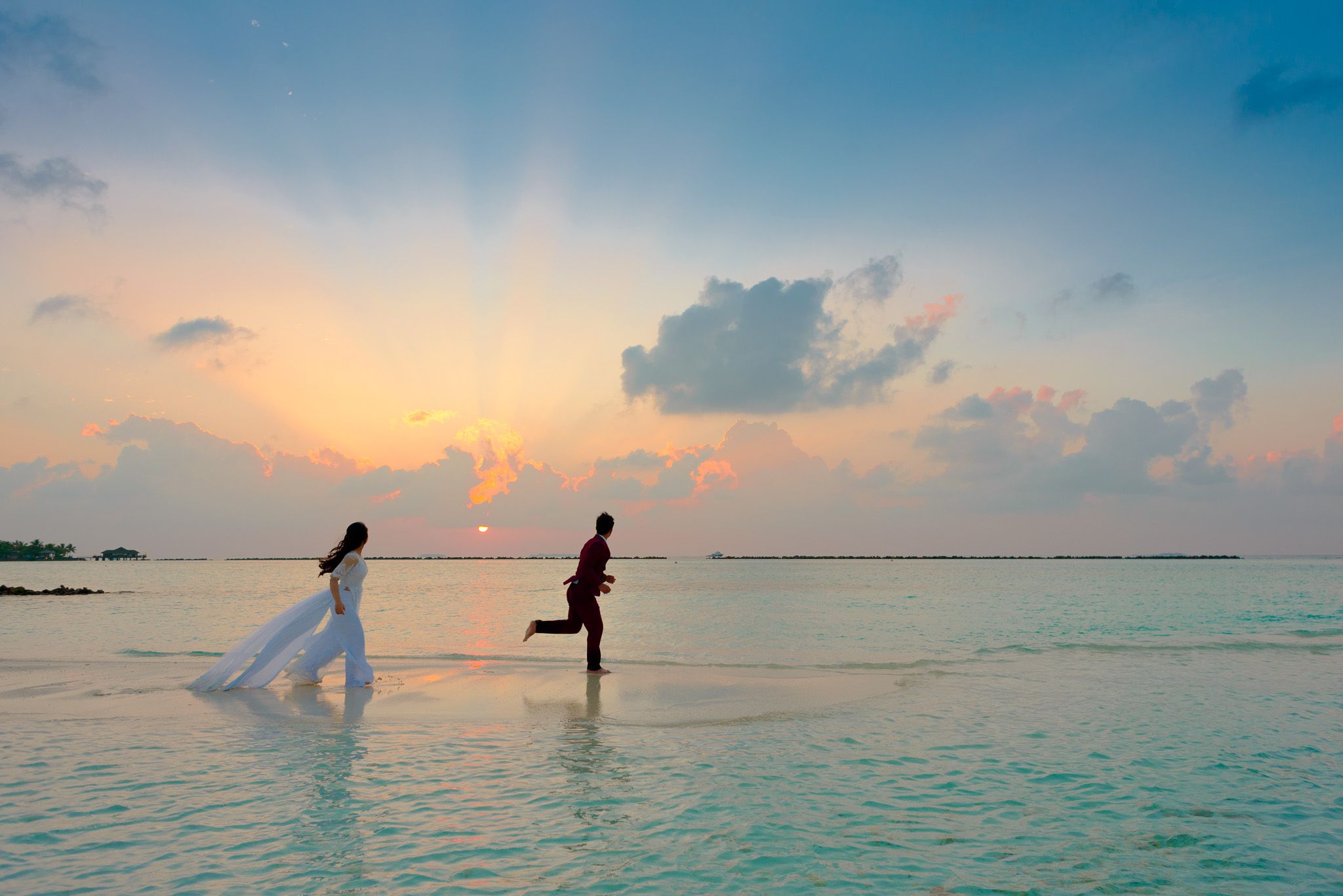 Bride and groom running barefoot across the shallows at sunset