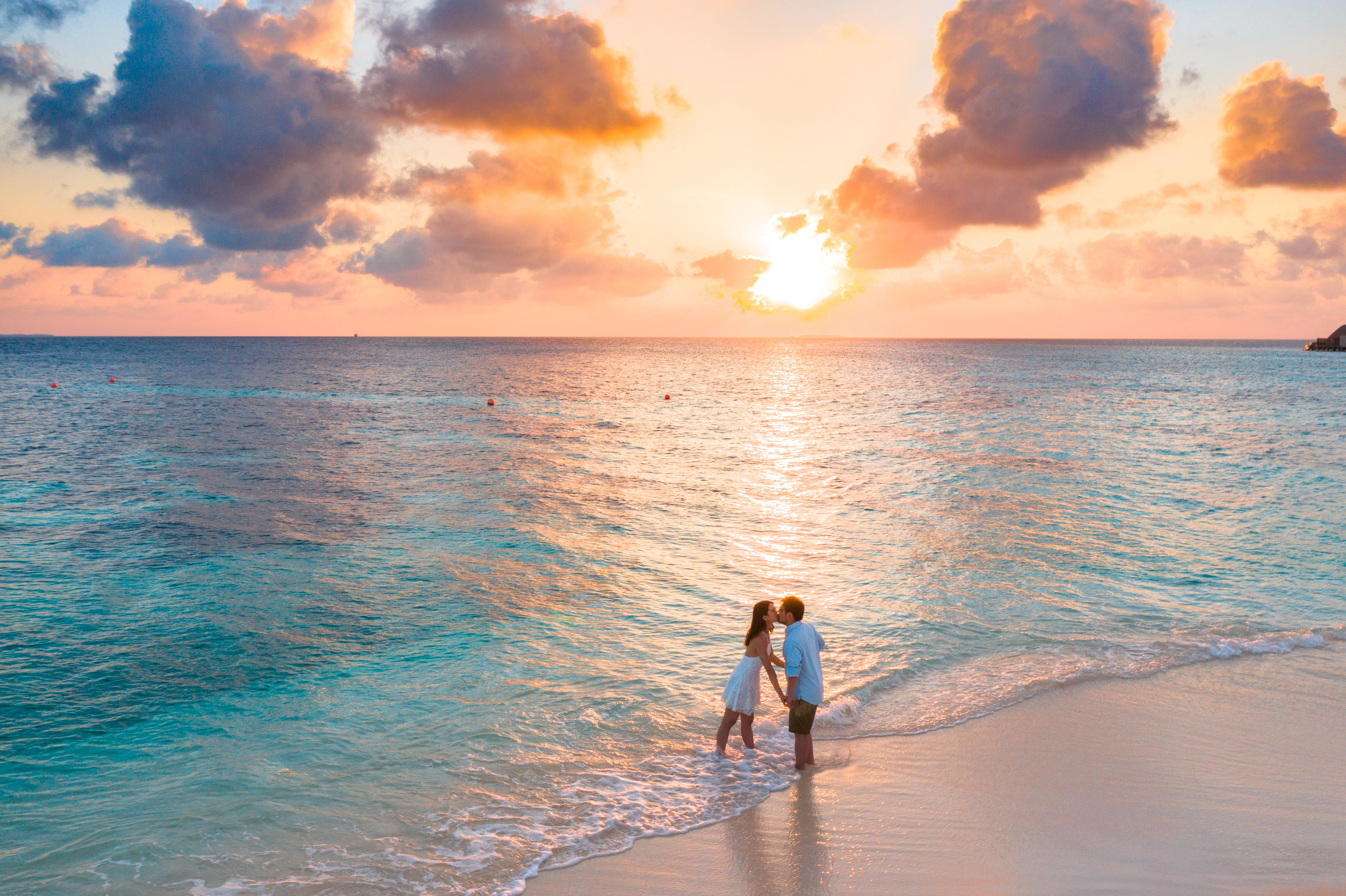 Couple kissing at the water’s edge on a beach at sunset