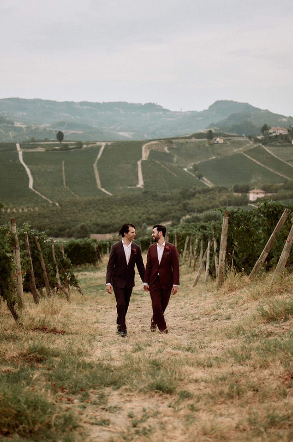 Two grooms walking hand in hand along a path through the vineyards